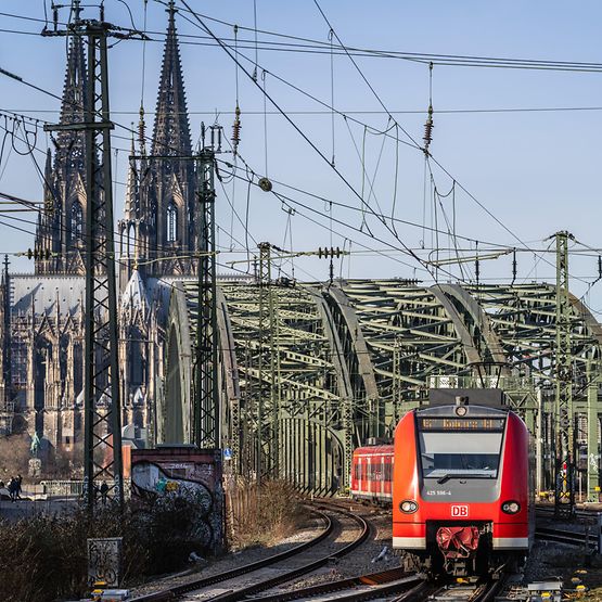 Ein S-Bahnzug auf der Hohenzollernbrücke in Köln. Im Hintergrund ist der Dom zu sehen.
