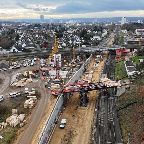 Vogelperspektive auf eine Bahnbaustelle. Zwei Brücken und Gleise sind zu sehen. Am Horizont ist die Bonner Skyline zu erkennen.