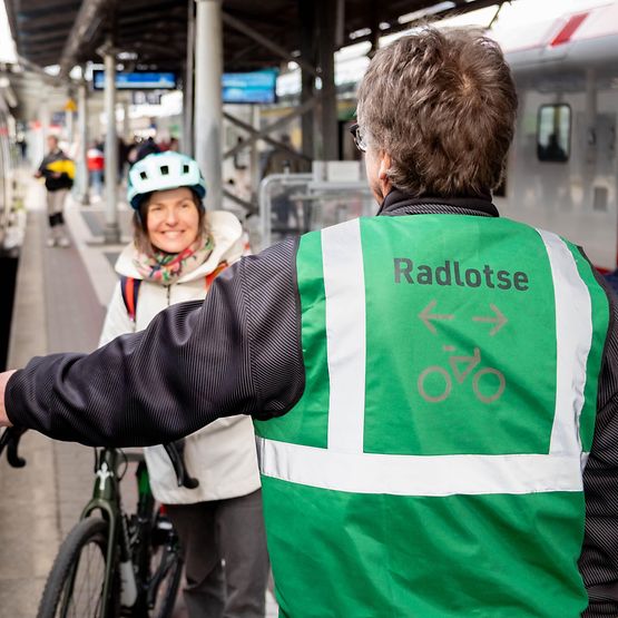 Radlotse hilft Radfahrerin am Bahnsteig beim Einstieg