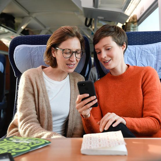 zwei Frauen sehen im Zug aufs Handy