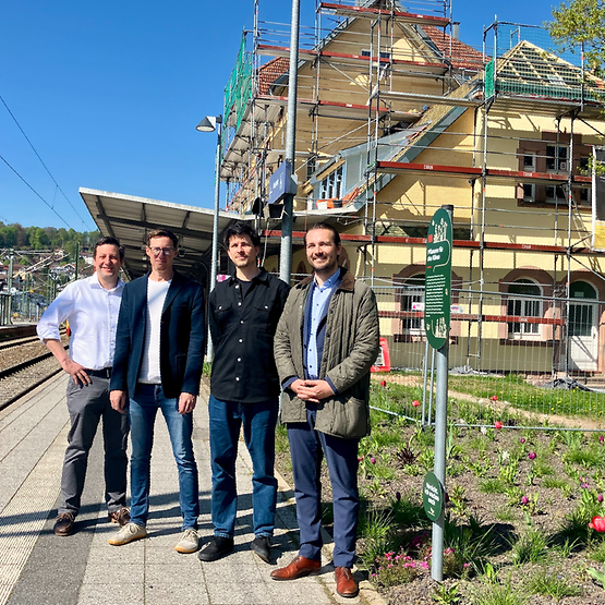 Vier Männer stehen am Bahnsteig. Im Hintergrund der Bahnhof Freudenstadt