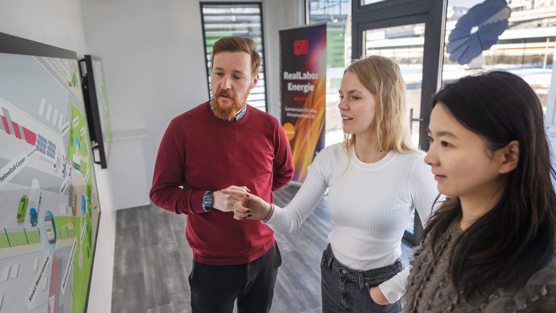 Drei Menschen stehen an einem Bildschirm im Showroom des DB Reallabor Energie.