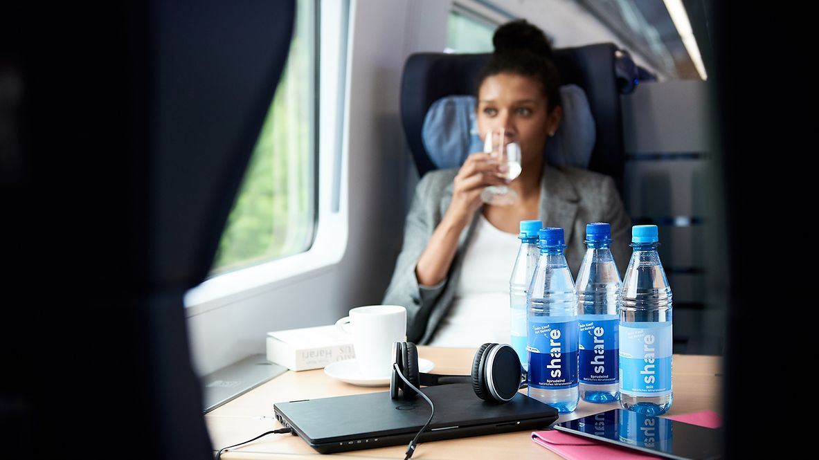 In einem DB-Zug trinkt eine Reisende Wasser aus einer share-Flasche.