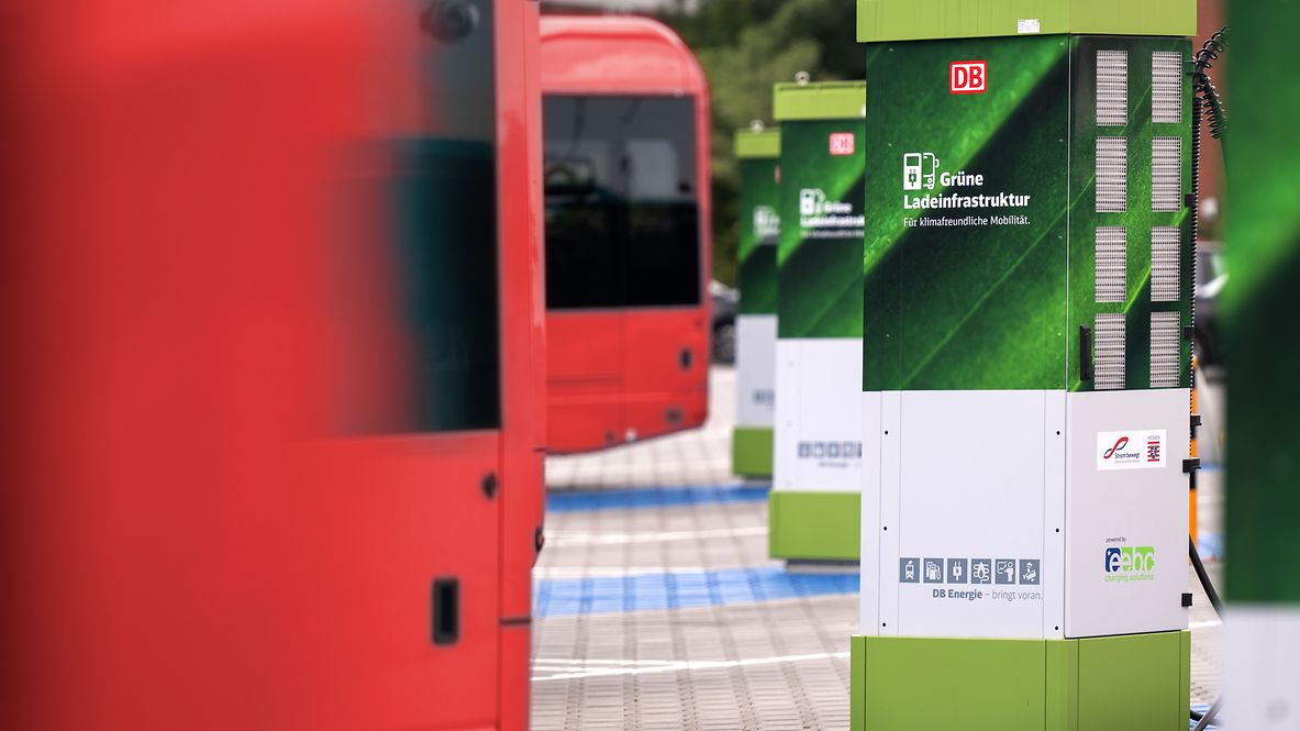 A green charging station next to red electric buses at the station.