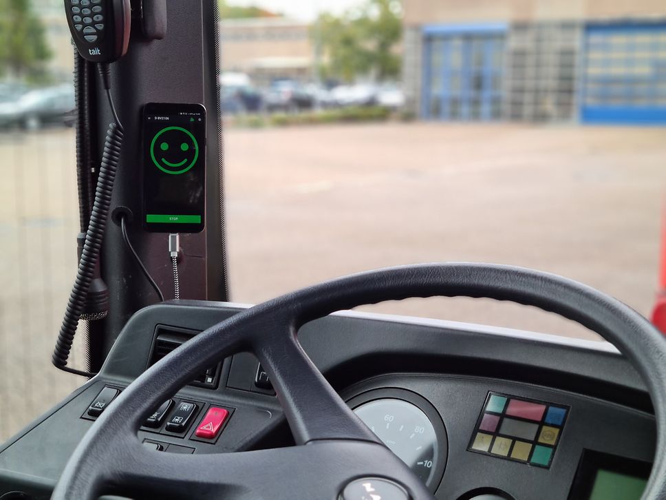 View of a steering wheel and dashboard, next to a phone showing a green smiley face on its screen.