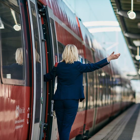 Eine Zugbegleiterin in der Tür eines Regionalzuges am Bahnhof